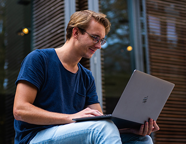 young person using a laptop sat outside what looks like a modern office