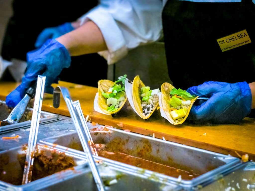 A chef prepares tacos whilst wearing blue plastic gloves.
